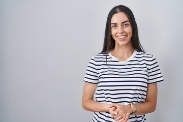 Young brunette woman wearing striped t shirt with hands together and crossed fingers smiling relaxed and cheerful. success and optimistic