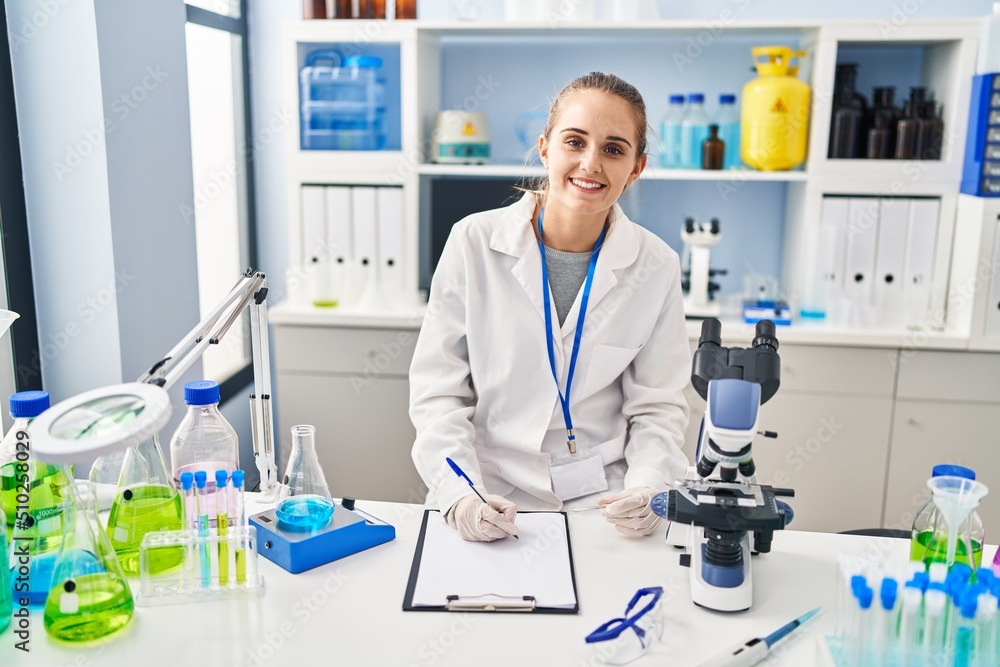 Poster young blonde woman wearing scientist uniform writing on checklist at laboratory