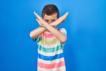 Young caucasian kid standing over blue background rejection expression crossing arms doing negative...
