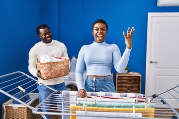 Young african american couple hanging clothes at clothesline celebrating victory with happy smile and winner expression with raised hands