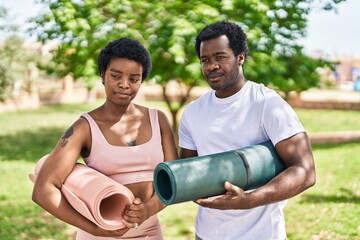 African american man and woman couple holding yoga mat with relaxed expression at park