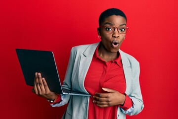Young african american woman holding laptop scared and amazed with open mouth for surprise,...