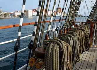 Obraz premium Closeup of a row of tied ropes on a retro tall ship, Willemstad skyline in the background