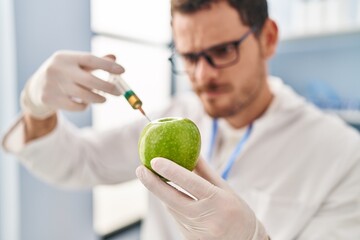 Young hispanic man scientist injecting liquid on apple at laboratory