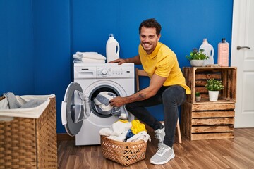 Young hispanic man smiling confident washing clothes at laundry room