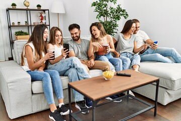 Group of young friends smiling happy and using smartphone sitting on the sofa at home.