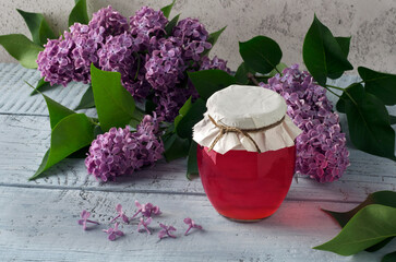 Lilac flowers syrup in glass jar and lilac blossoms on wooden table.