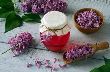 Lilac flowers syrup in glass jar and lilac flower petals on wooden table.