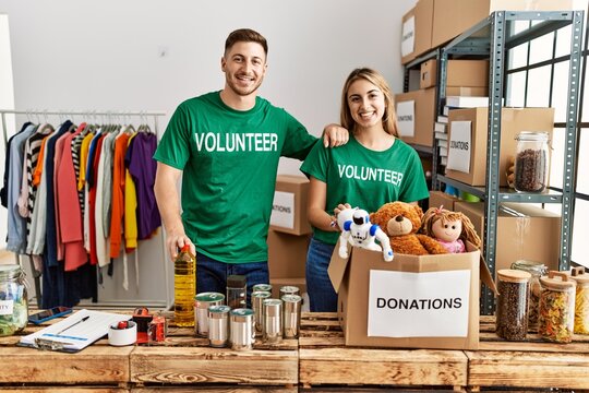 Young hispanic volunteer couple smiling happy standing at charity center.