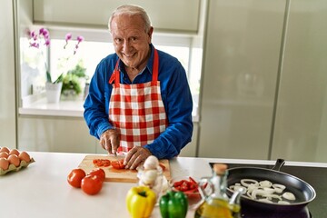Senior man smiling confident cutting tomato at kitchen