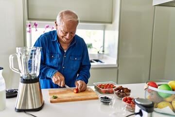 Senior man smiling confident cutting strawberry at kitchen