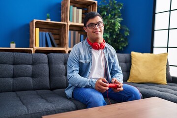 Down syndrome man playing video game sitting on sofa at home