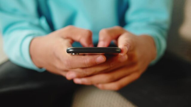 African American man using smartphone. Young guy texting at phone, teenager relaxing at home. Communicating with family and friends online, sitting on sofa in living room.