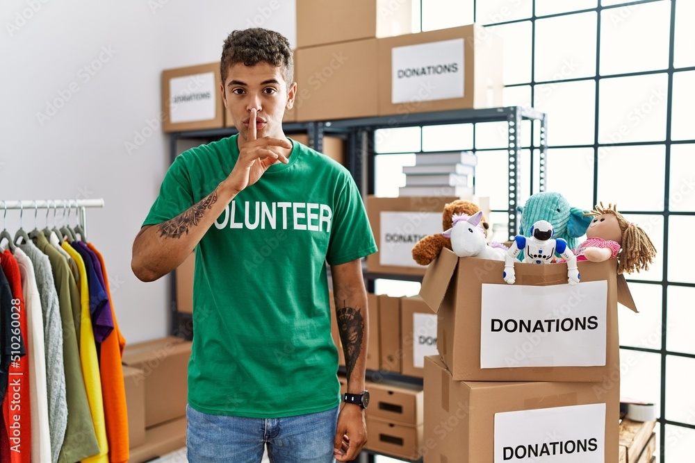 Sticker young handsome hispanic man wearing volunteer t shirt at donations stand asking to be quiet with fin