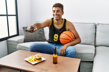 Young hispanic man watching basketball game on tv at home