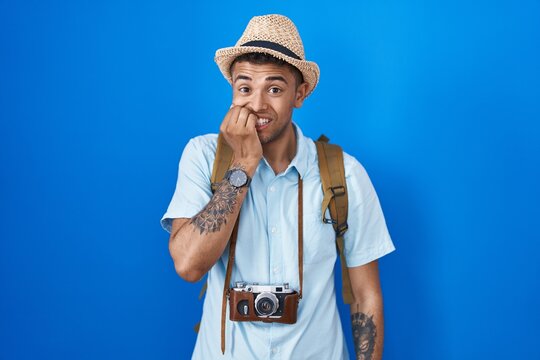 Brazilian young man holding vintage camera looking stressed and nervous with hands on mouth biting nails. anxiety problem.