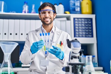 Young hispanic man scientist smiling confident holding test tubes at laboratory