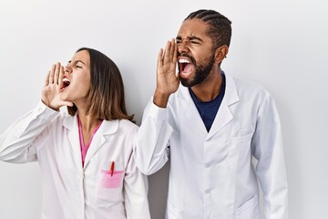 Young hispanic doctors standing over white background shouting and screaming loud to side with hand on mouth. communication concept.