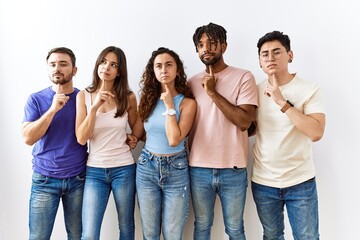 Obraz premium Group of young people standing together over isolated background thinking concentrated about doubt with finger on chin and looking up wondering