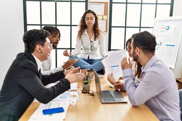 Businesswoman enjoys meditating during meeting. Sitting on desk near arguing partners at the office.