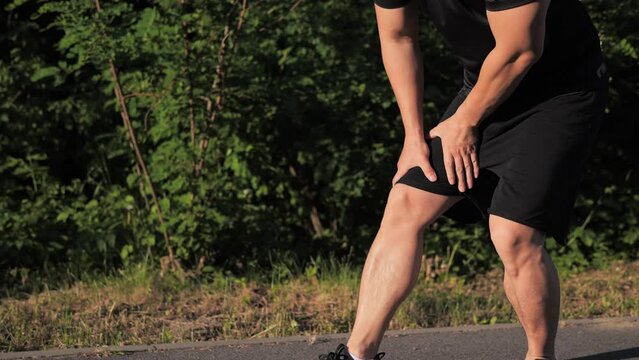 Sportive asian runner athlete running and suddenly feels pain cramps in the leg at sunset. Man stops massaging knee stretching, trauma injury while jogging outdoors. Sprain severe pain stretch pull.
