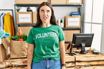 Young brunette woman wearing volunteer t shirt at donations stand angry and mad screaming frustrated and furious, shouting with anger. rage and aggressive concept.