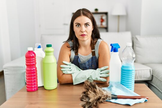 Young brunette woman wearing cleaner apron and gloves cleaning at home relaxed with serious expression on face. simple and natural looking at the camera.