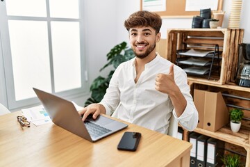 Young arab man working using computer laptop at the office smiling happy and positive, thumb up...