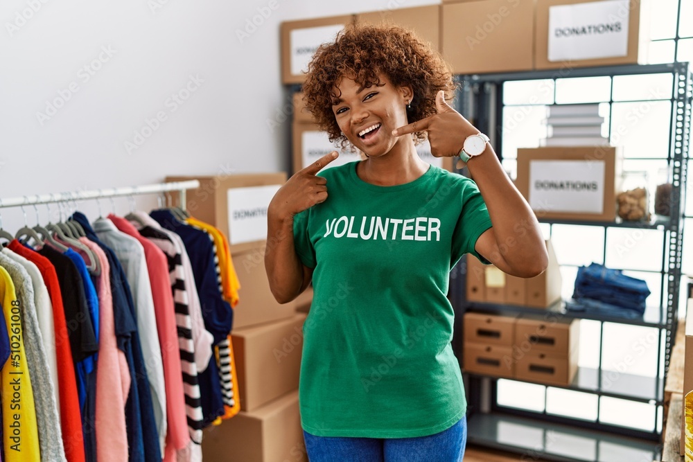 Sticker Young african american woman wearing volunteer t shirt at donations stand smiling cheerful showing and pointing with fingers teeth and mouth. dental health concept.