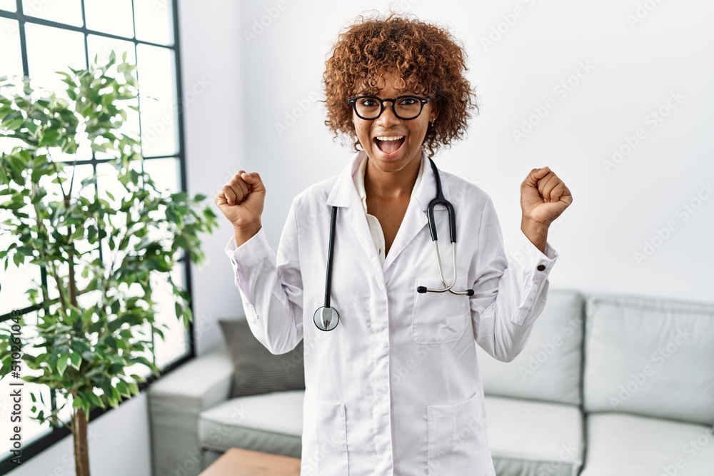 Canvas Prints young african american woman wearing doctor uniform and stethoscope celebrating surprised and amazed