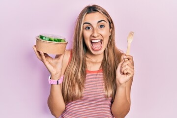 Beautiful hispanic woman eating salad celebrating crazy and amazed for success with open eyes...