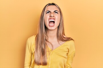 Beautiful hispanic woman wearing casual yellow sweater angry and mad screaming frustrated and...