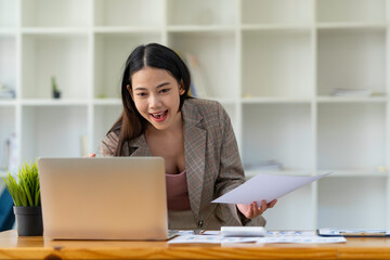Happy Asian woman office worker feeling excitement raising fists celebrates career ladder promotion or reward, businesswoman sitting at desk receive online news, great results successful work concept