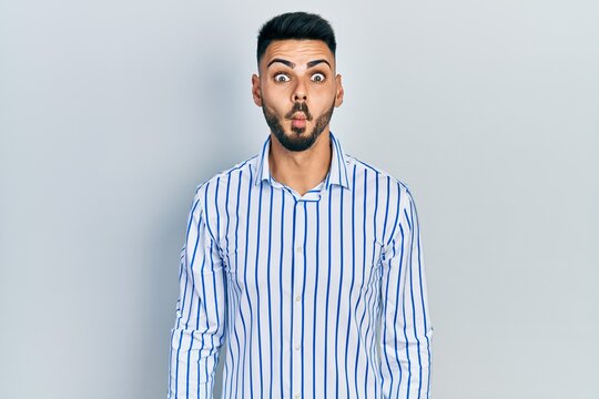 Young hispanic man with beard wearing casual striped shirt making fish face with lips, crazy and comical gesture. funny expression.