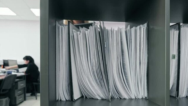 Office worker takes a folder with documents from the document rack and goes with it to her workplace. Close-up view of folder with documents