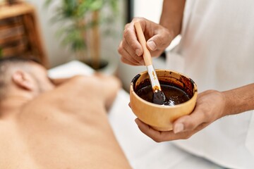 Two hispanic men physiotherapist and patient having skin back treatment using exfoliating lotion at...