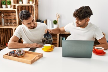 Two hispanic men couple pouring coffee having breakfast at home