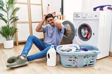 Young hispanic man putting dirty laundry into washing machine posing funny and crazy with fingers on head as bunny ears, smiling cheerful