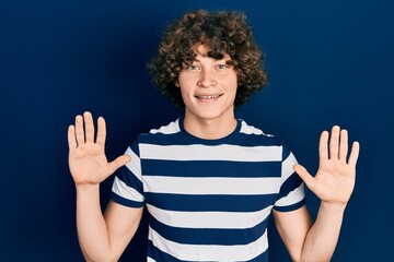 Handsome young man wearing casual striped t shirt showing and pointing up with fingers number ten while smiling confident and happy.