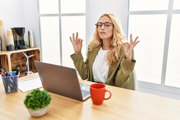 Beautiful blonde woman working at the office with laptop relax and smiling with eyes closed doing meditation gesture with fingers. yoga concept.