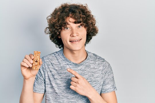 Handsome young man eating protein bar as healthy energy snack smiling happy pointing with hand and finger