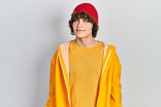 Handsome young man wearing yellow raincoat looking away to side with smile on face, natural expression. laughing confident.