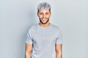 Young hispanic man with modern dyed hair wearing casual grey t shirt with a happy and cool smile on...