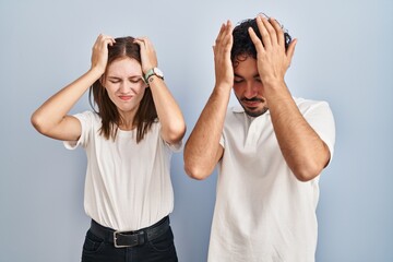 Young couple wearing casual clothes standing together suffering from headache desperate and stressed because pain and migraine. hands on head.