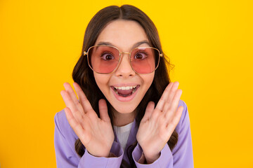 Amazed teen girl. Excited expression, cheerful and glad. Headshot portrait of cute teenager child girl isolated on yellow studio background wear sunglasses look at camera.