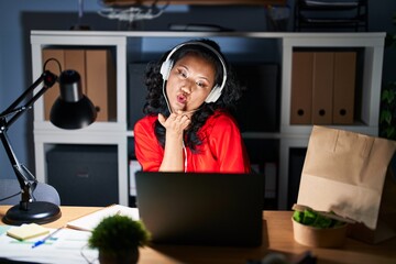 Young asian woman working at the office with laptop at night looking at the camera blowing a kiss with hand on air being lovely and sexy. love expression.