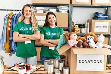 Two young volunteers woman smiling happy standing with arms crossed gesture at charity center.