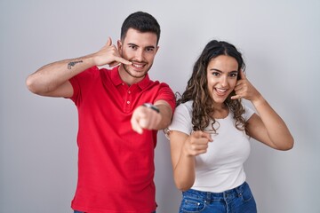 Young hispanic couple standing over isolated background smiling doing talking on the telephone...