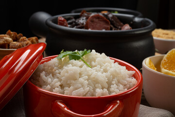 .White rice in the foreground, served in a clay bowl and blurred feijoada in the background