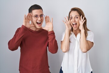 Mother and son standing together over isolated background smiling cheerful playing peek a boo with hands showing face. surprised and exited